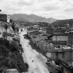 View of town of Otovalo, Ecuador with housing construction, church, and people and dog walking along dirt road.